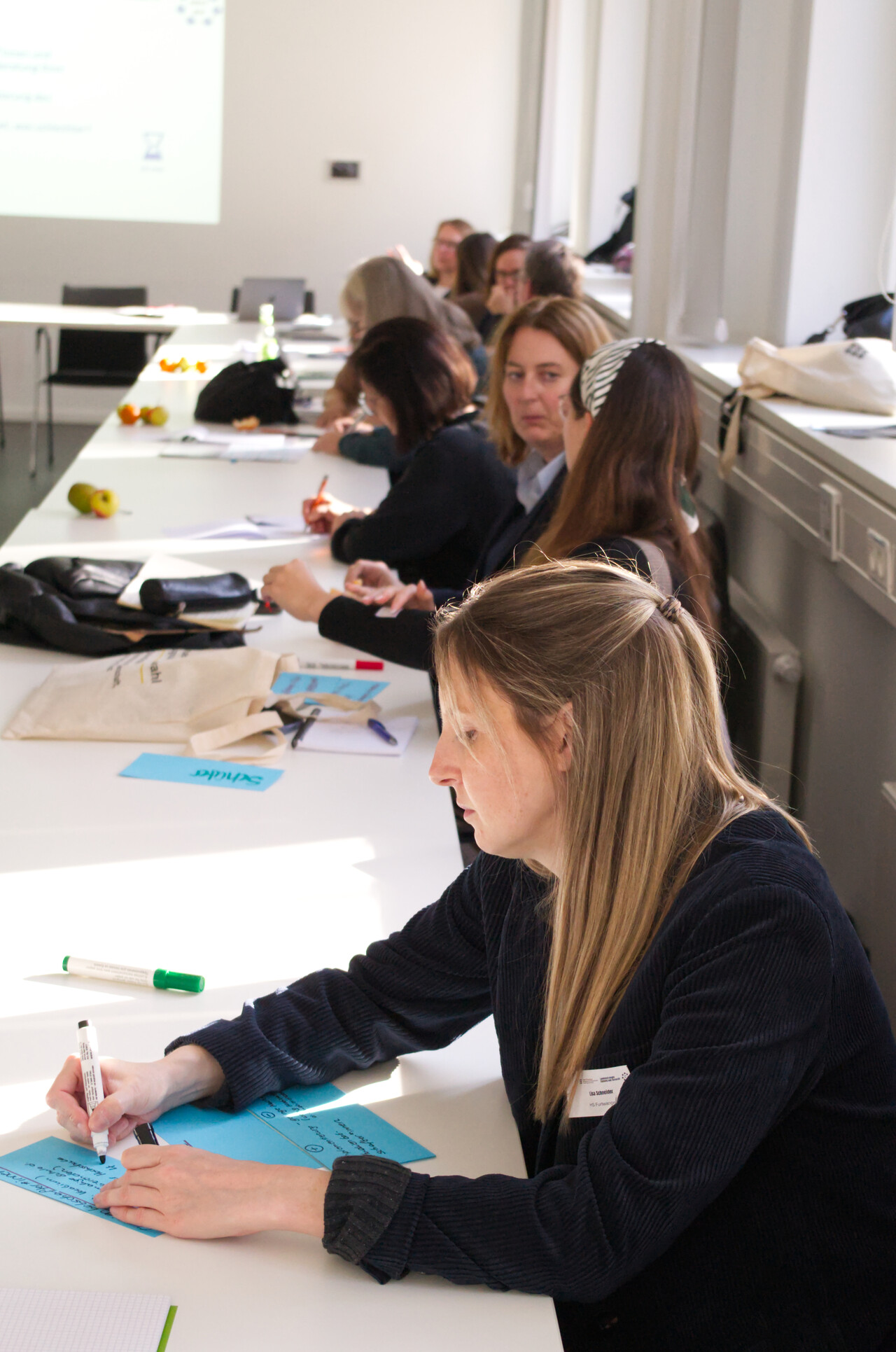 Eine Teilnehmerin schreibt Diskussionsergebnisse mit einem Marker auf buntes Papier.