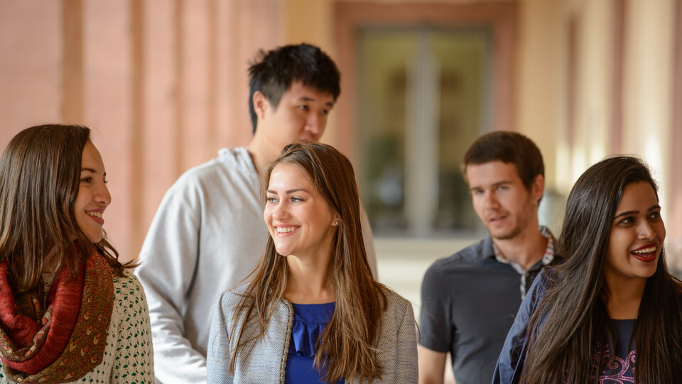 Drei Studentinnen und zwei Studenten laufen einen Gang der Universität entlang.