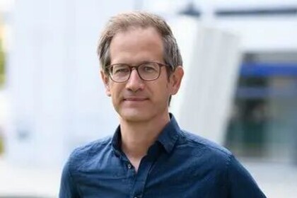 Portrait von Marc Helbling. Er trägt ein blaues Hemd und steht auf einer Grünfläche.