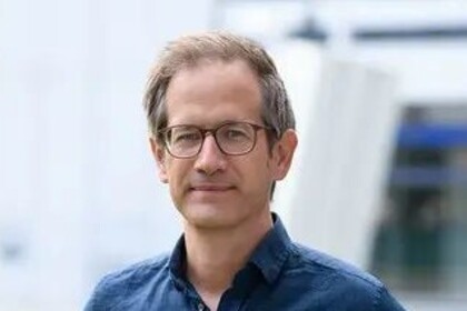 Portrait von Marc Helbling. Er trägt ein blaues Hemd und steht auf einer Grünfläche.