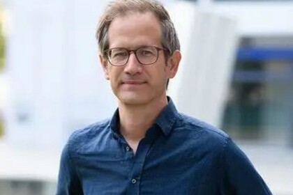 Portrait von Marc Helbling. Er trägt ein blaues Hemd und steht auf einer Grünfläche.
