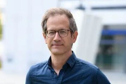 Portrait von Marc Helbling. Er trägt ein blaues Hemd und steht auf einer Grünfläche.