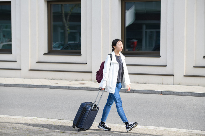 A doctoral student is walking in front of the B6, 30-32 building with a suitcase.