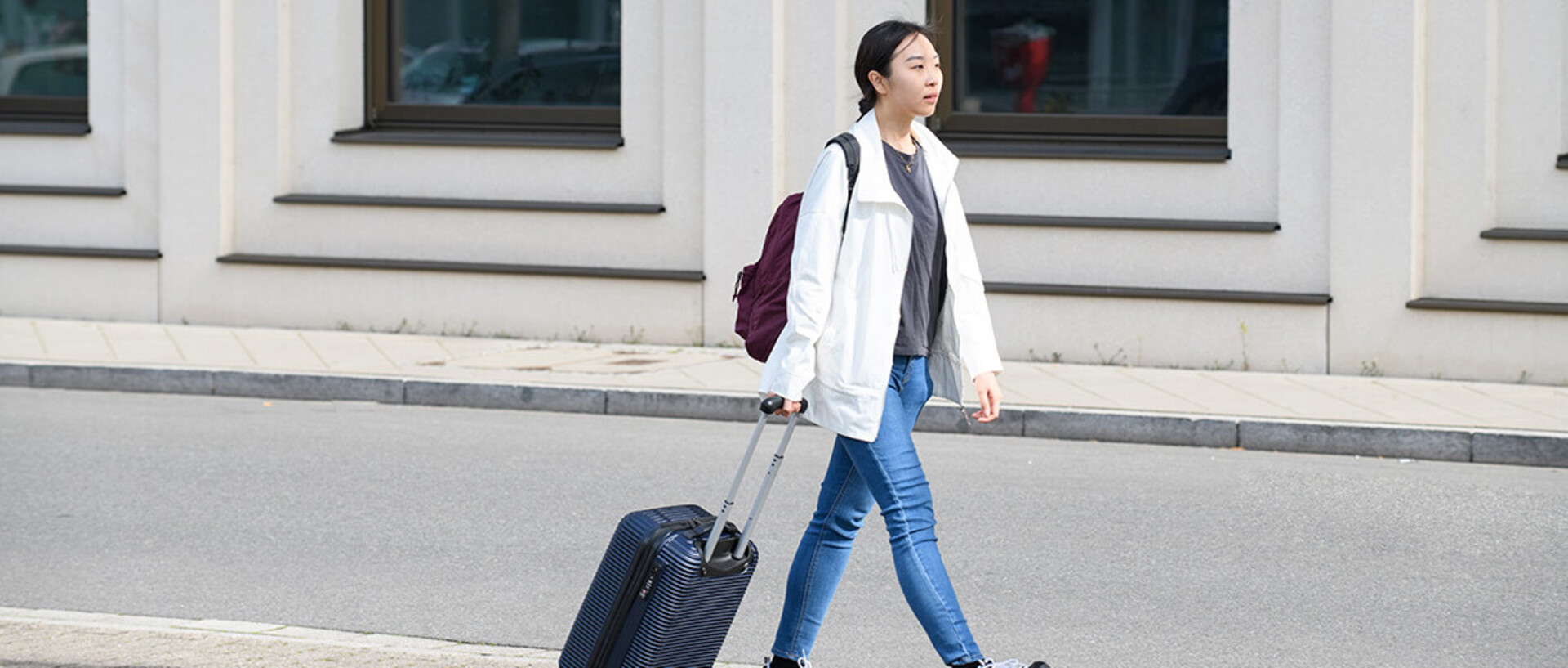 A doctoral student is walking in front of the B6, 30-32 building with a suitcase.