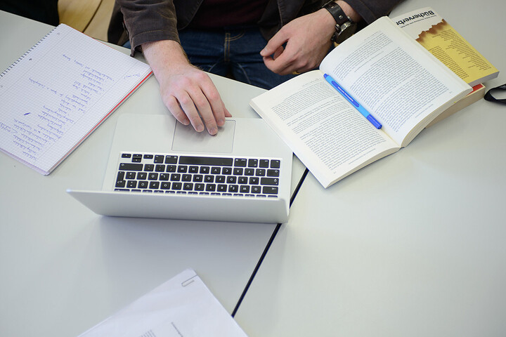 Ein Student sitzt mit Büchern und seinem Laptop an einem Tisch.