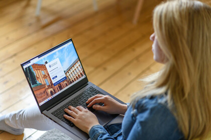Person hat einen Laptop auf dem Schoß, beide Hände liegen auf der Tastatur, man sieht die Anmeldemaske der Universität Mannheim.