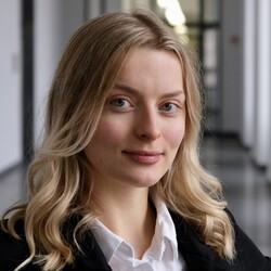 Porträt von Felicitas Holl. Felicitas Holl trägt einen schwarzen Blazer und eine weiße Bluse. Sie hat schulterlange blonde Haare und blaue Augen. Sie schaut selbstbewusst direkt in die Kamera. 