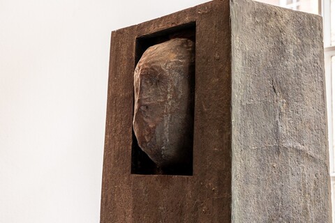 Bronzeplastik: Ein Gesicht ragt teilweise aus einem quaderförmige Block.