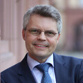 Eine Person trägt ein hellblaues Hemd. eine blau gemusterte Krawatte sowie einen dunkelblauen Blazer und steht vor dem Schloss der Universität Mannheim. Die Person heißt Ralf Müller-Terpitz. 