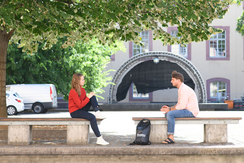 Zwei Studierende sitzen auf zwei Bänken im Schneckenhof.