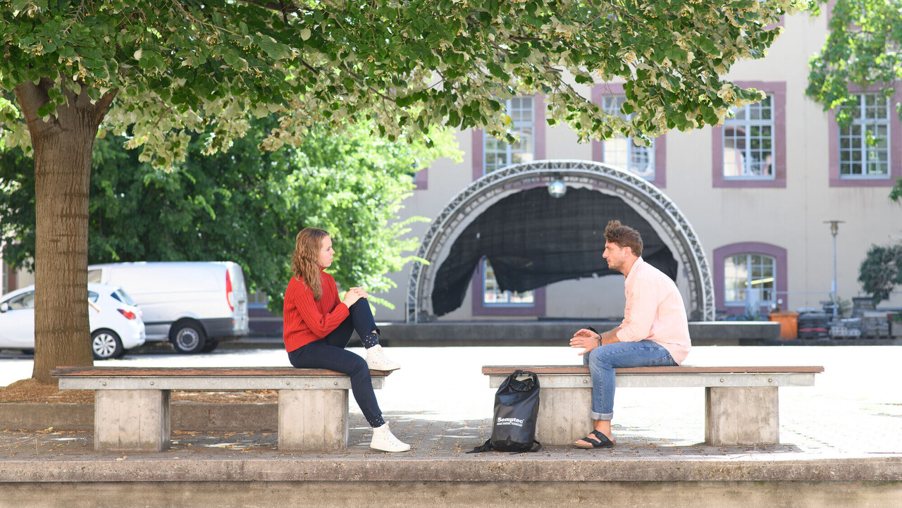 Zwei Studierende sitzen auf zwei Bänken im Schneckenhof.