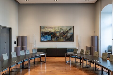 In einem Saal hängt ein großformatiges abstraktes Gemälde in Braun-, Blau und Grautönen und Streifen roter Farbe.
