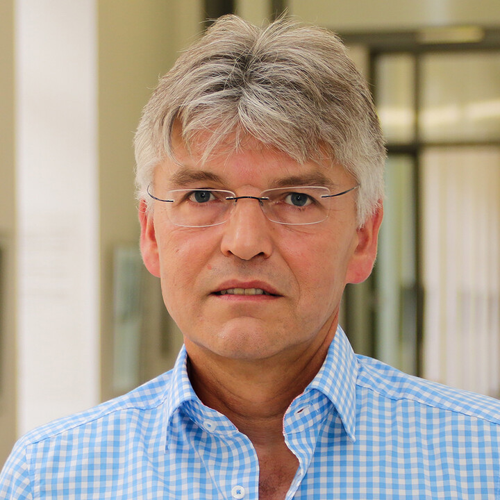 Portraitfoto eines Mannes mit Brille und blau-weiß kariertem Hemd.