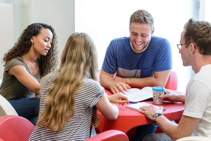 Vier Studierende sitzen an einem roten, runden Tisch und lernen gemeinsam.