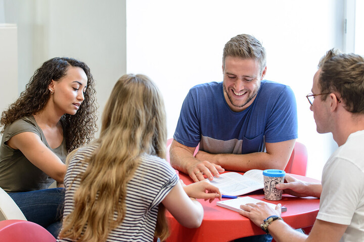 Vier Studierende sitzen an einem roten, runden Tisch und lernen gemeinsam.