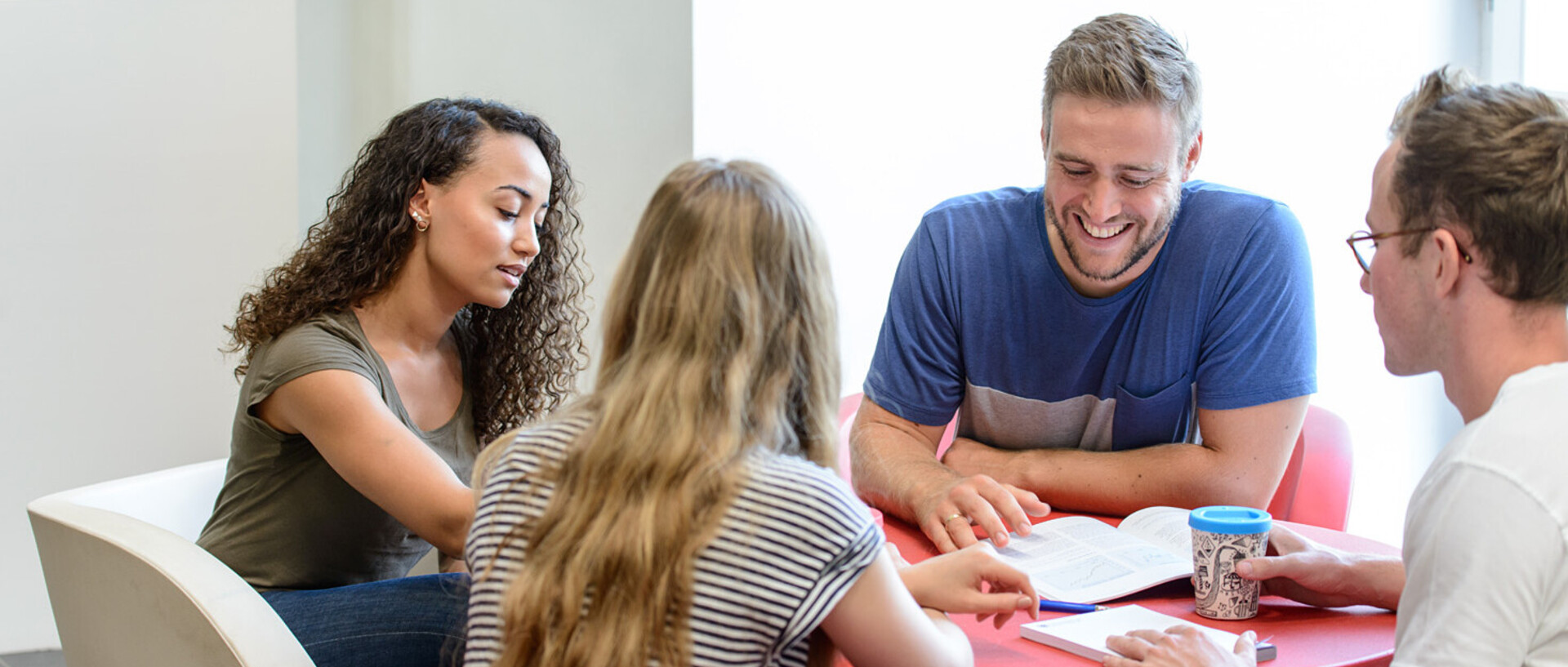 Vier Studierende sitzen an einem roten, runden Tisch und lernen gemeinsam.