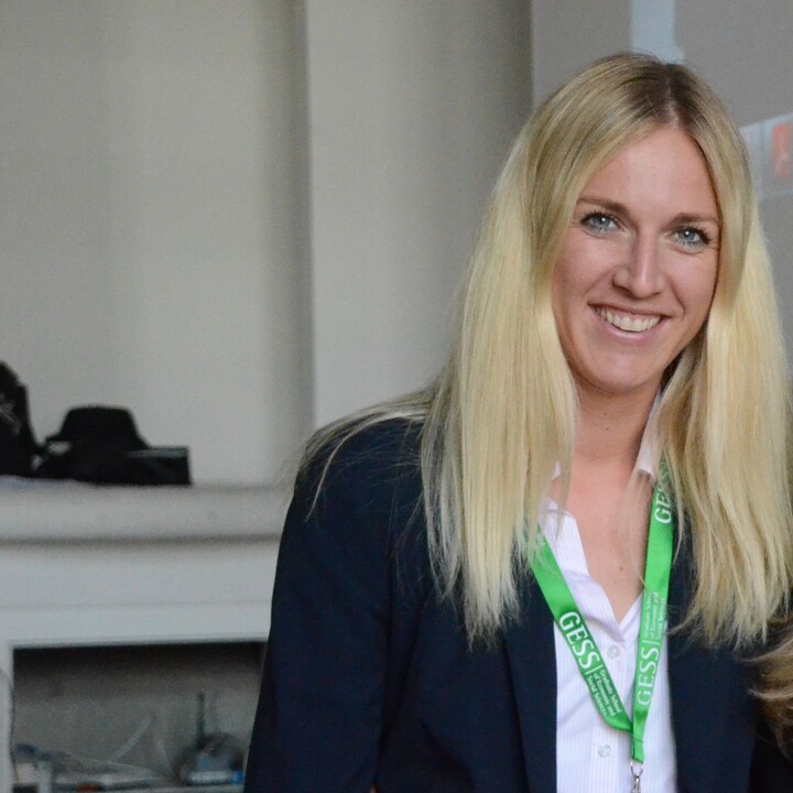 Eine Frau mit langen blonden Haaren blickt lächelnd in die Kamera.