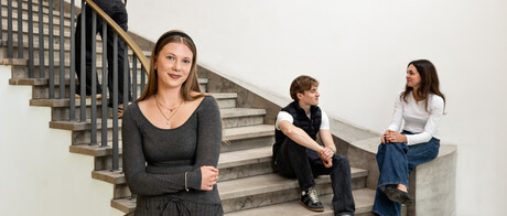 Eine Studentin steht im Treppenhaus des Schlosses. Drei Studierende sind im Hintergrund zu sehen. 
