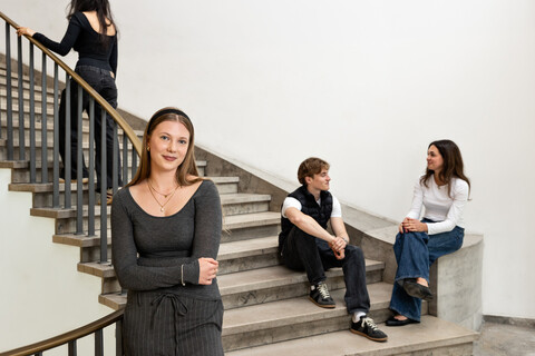 Eine Studentin steht im Treppenhaus des Schlosses. Drei Studierende sind im Hintergrund zu sehen. 