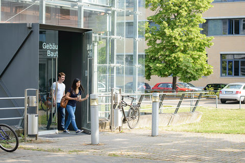 Ein Student und eine Studentin verlassen ein modernes, gläsernes Universitätsgebäude.