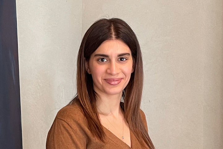 Alumna Armik Yordekyan trägt eine braune Weste, hat lange dunkle Haare und lächelt.