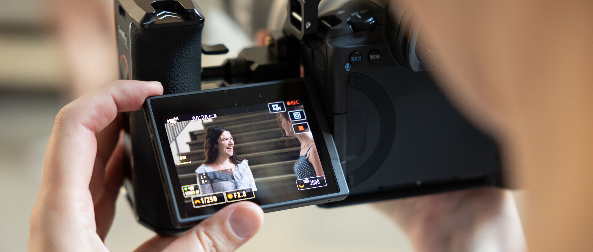 Spiegelreflexkamera, auf deren Display ein Bild von zwei lachenden Studierenden angezeigt wird