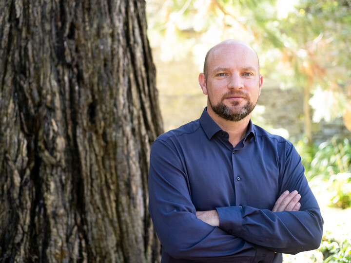 Prof. Ulrich Wagner. Er steht freundlich dreinblickend in blauem Hemd vor einem Baum.