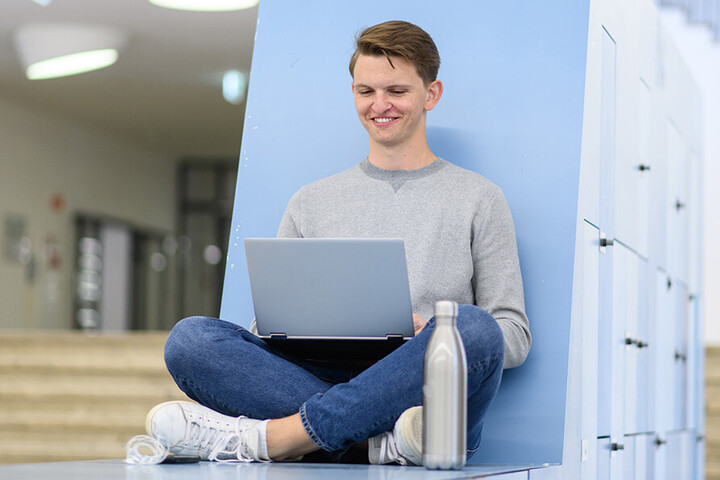 Ein Student sitzt mit seinem Laptop in einem Aufenthaltsbereich der Universität Mannheim.