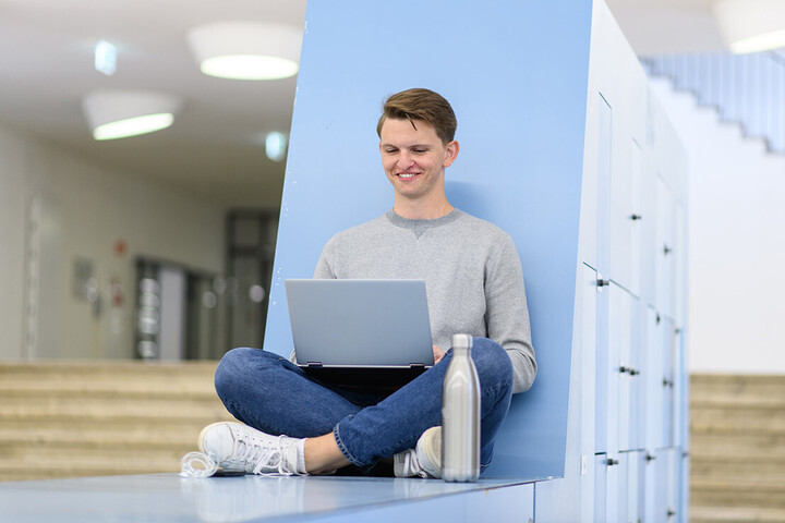 Ein Student sitzt mit seinem Laptop in einem Aufenthaltsbereich der Universität Mannheim.