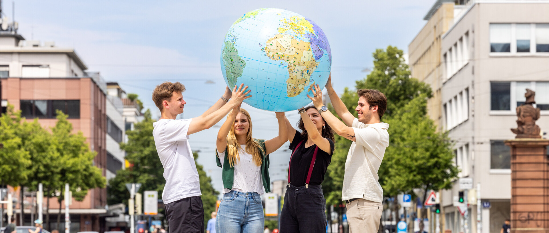 Vier Studierende stehen auf dem Ehrenhof und halten einen Globus in die Höhe. Im Hintergrund ist Mannheim zu sehen.