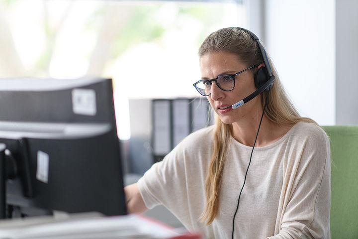 Mitarbeiterin mit Headset arbeitet konzentriert am Computer.