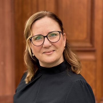 Porträtfoto einer Frau, leicht seitlich zur Kamera gedreht und mit bräunlichem Hintergrund.