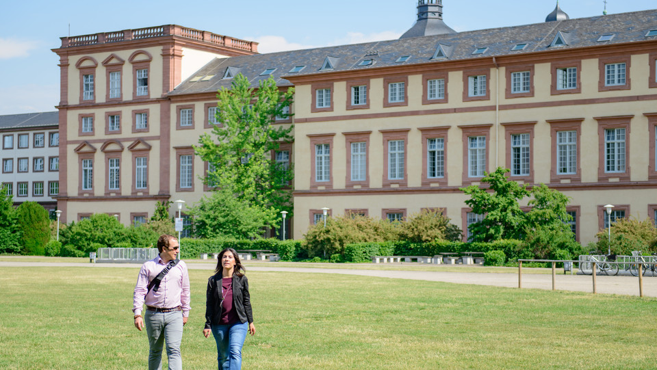 Zwei Personen laufen über die Wiese vor dem Mannheimer Schloss, dem Sitz der Universität Mannheim