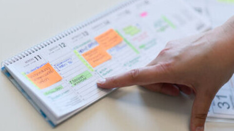 Eine Hand zeigt auf einen Kalender mit verschiedenen Terminen