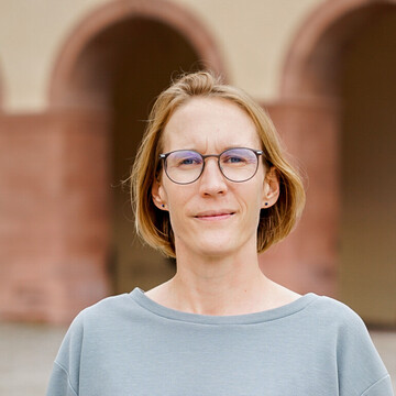 Portraitaufnahme von Regine Zeller im Ehrenhof des Mannheimer Schlosses, Regine Zeller hat halblange braune Haare, trägt eine Brille und einen grauen Pullover