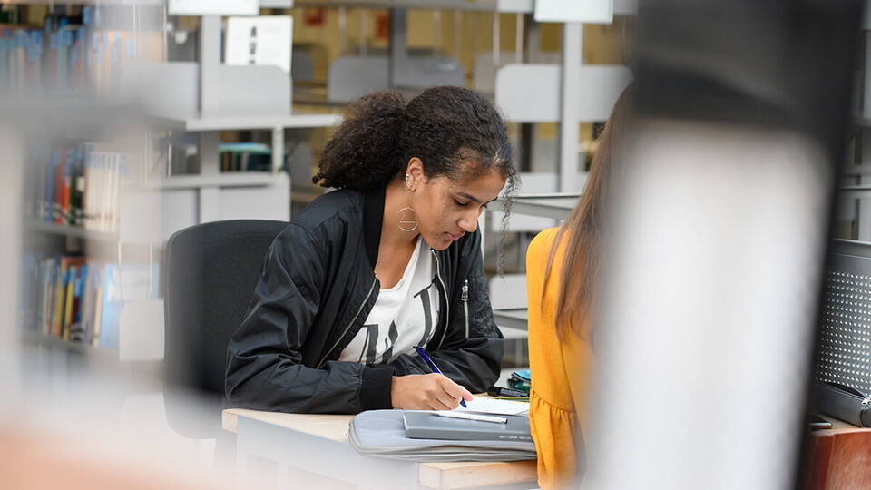 Eine Studentin in der Bibliothek schreibt am Laptop