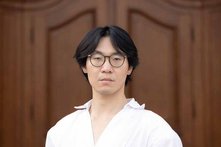 Portrait of Mingjie Xu. He is wearing a white shirt and standing in front of a door.