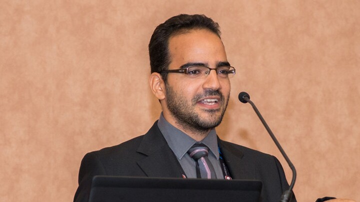 Muhammad Muhammad standing at lectern, dark jacket, shirt and tie