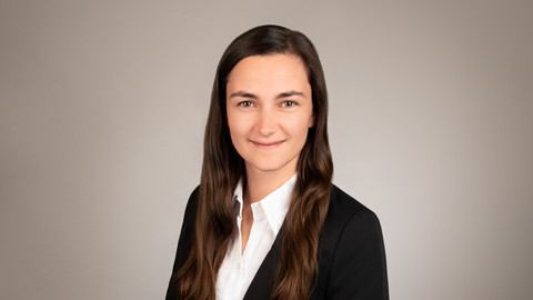 Leonie Gehrmann. She is wearing a black jacket over a white blouse and is standing in front of a brown wall.