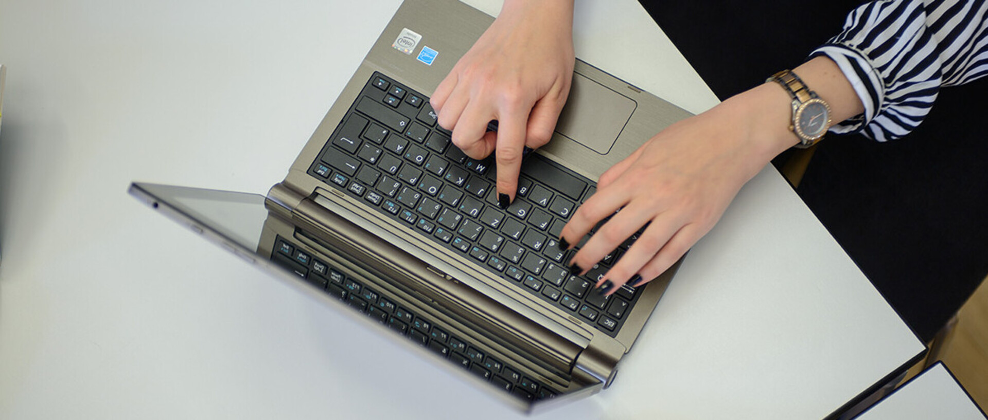 Zwei Hände tippen auf einem Laptop.