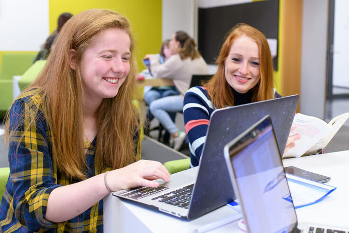 Zwei Studentinnen blicken lachend auf einen Laptop.