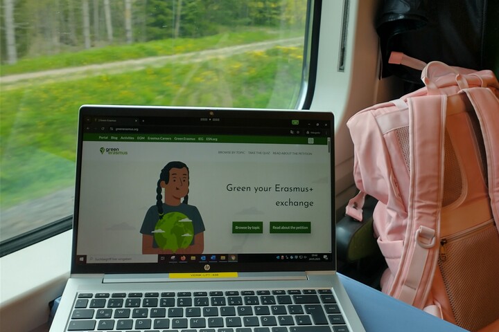 Ein Laptop am Zugfenster. Auf dem Display: "Green your Erasmus+ Exchange"