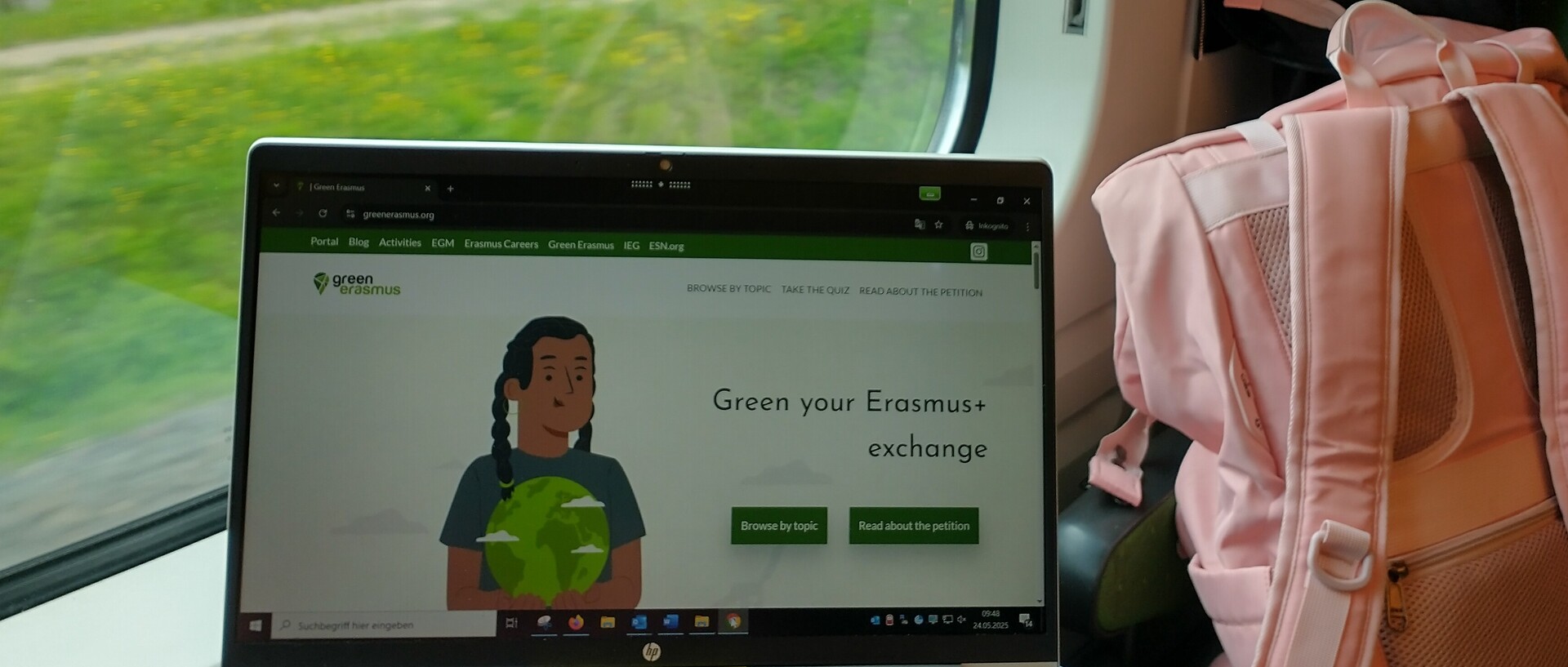 Ein Laptop am Zugfenster. Auf dem Display: "Green your Erasmus+ Exchange"