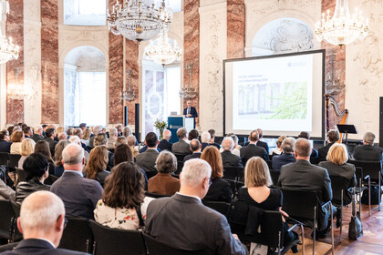 Blick in den vollbesetzten Rittersaal. Auf der Bühne ist eine Präsentation zu sehen und der Rektor am Rednerpult.