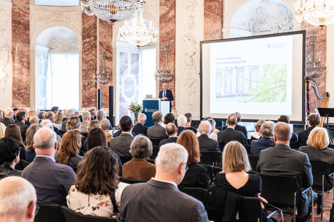 Blick in den vollbesetzten Rittersaal. Auf der Bühne ist eine Präsentation zu sehen und der Rektor am Rednerpult.