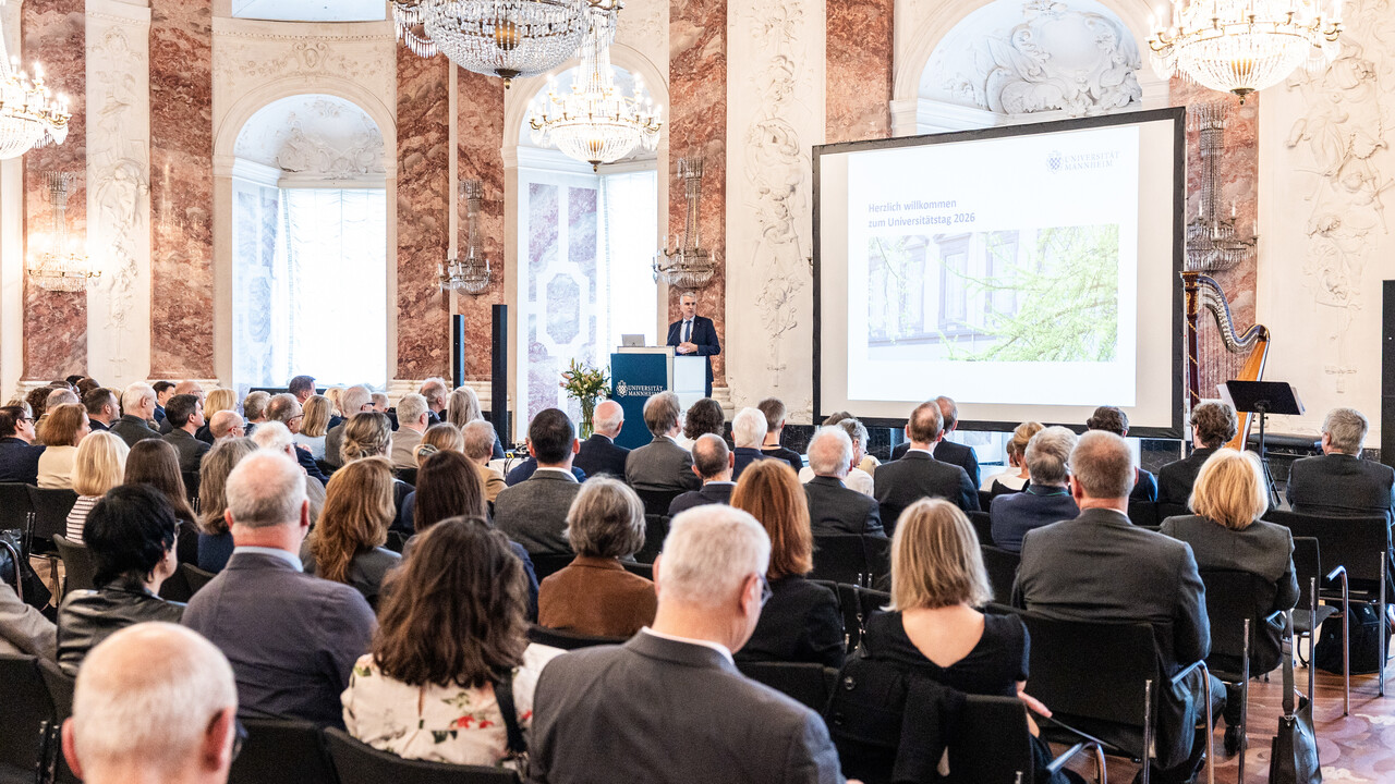 Universitätstag 2026 Blick in den vollbesetzten Rittersaal. Auf der Bühne ist eine Präsentation zu sehen und der Rektor am Rednerpult.