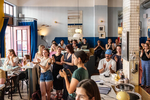Publikum in Café applaudiert nach Veranstaltung, einige stehen, andere sitzen.