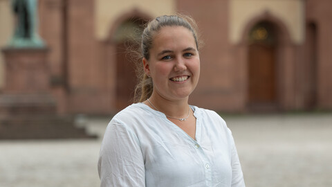 Lisa-Marie Werner. She is wearing a white shirt and is standing on the Ehrenhof in front of the castle.