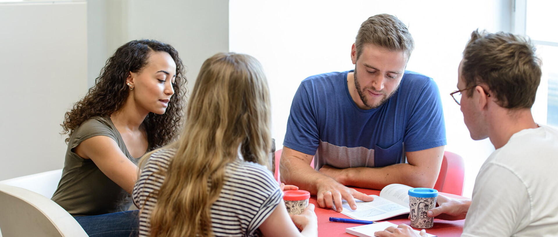 Vier Studierende sitzen an einem runden Tisch und lernen gemeinsam.