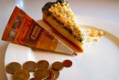 Ein Teller mit einem Stück Streuselkuchen, einem wie ein Stück Kuchen gefalteten 10 Euro Schein und einigen Münzen ebenfalls in der Form eines Kuchens auf den Teller gelegt.